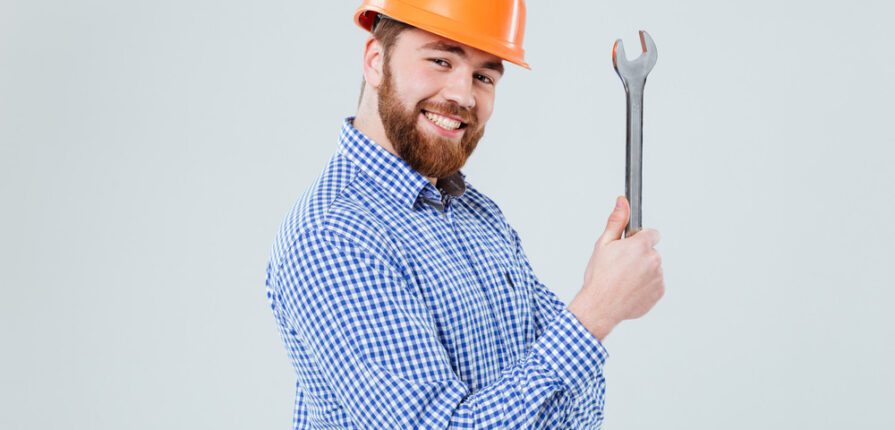 Smiling bearded young man in helmet with wrench