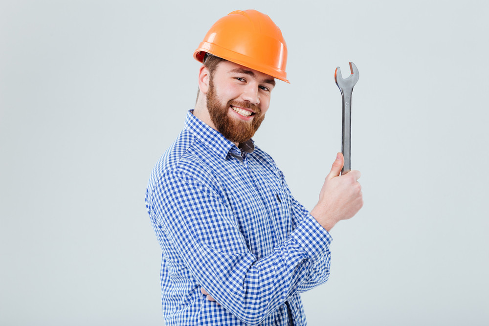 Smiling bearded young man in helmet with wrench